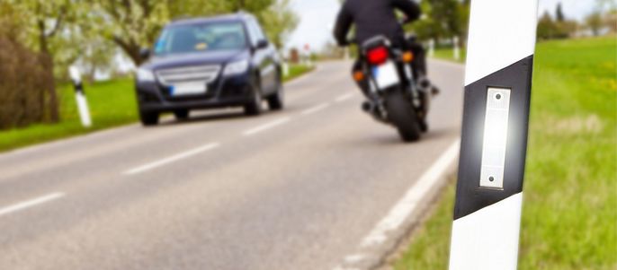 Eine Straße mit einem Motorrad und einem Auto, mit einer weißen Straßenmarkierung an der Seite.