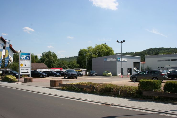 Ein Autohaus mit verschiedenen Fahrzeugen, die draußen geparkt sind, ein Schild mit dem Logo von TUEV Hessen und ein Gebäude mit der Aufschrift "SERVICE CENTER".