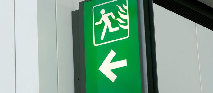 Ein grünes Zeichen mit einer weißen, laufenden menschlichen Figur und einem Flammensymbol, begleitet von einem weißen Pfeil, der nach rechts zeigt.