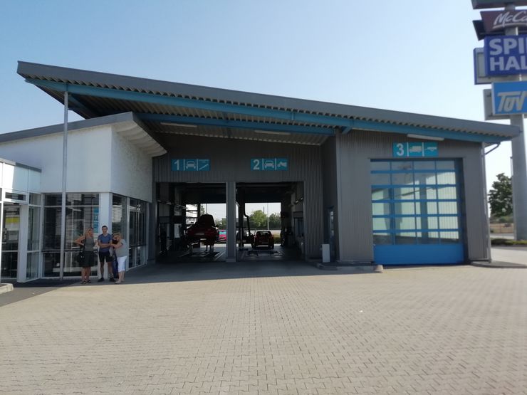 Eine moderne Autowaschanlage mit blau-weißer Fassade, zwei Personen, die draußen stehen.
