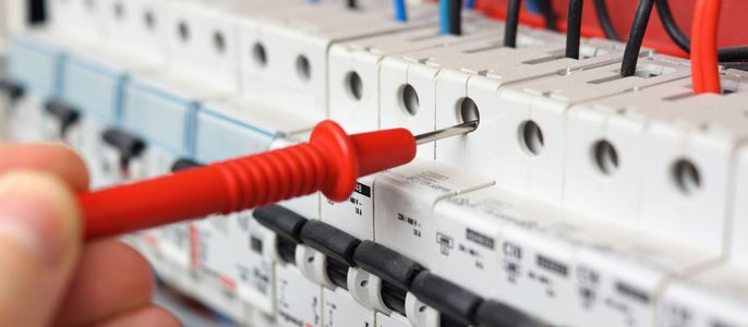 Eine elektrische Schalttafel mit mehreren angeschlossenen Drähten und einer Hand, die einen roten Schraubenzieher benutzt, um eine der Klemmen zu überprüfen.