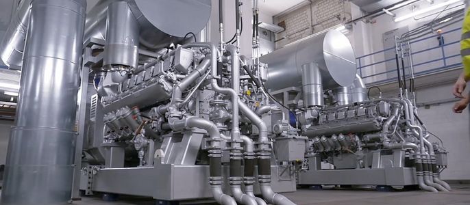 Eine große Industrieanlage mit zahlreichen Rohren und Ventilen, die sich in einem Raum mit hoher Decke und Metallstrukturen befindet.