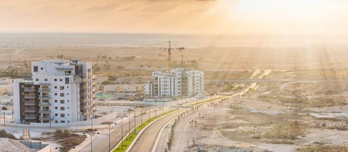 Eine moderne Stadtlandschaft bei Sonnenuntergang, mit mehreren im Bau befindlichen Gebäuden, einer kurvenreichen Straße und einer weiten Landschaft im Hintergrund.