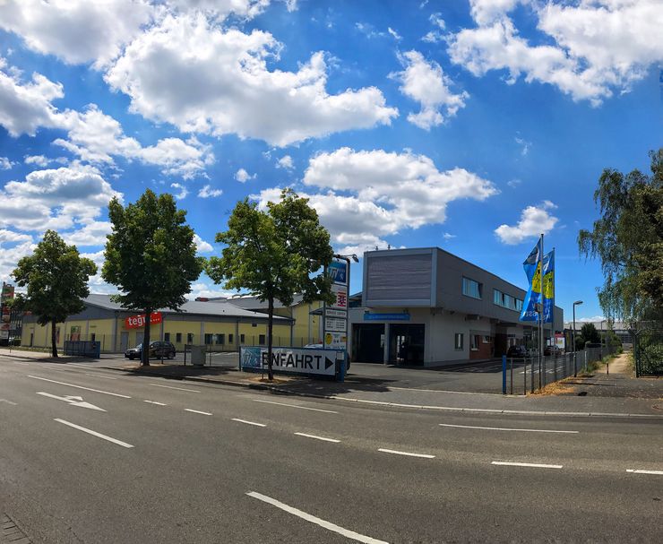 Eine Straßenansicht mit einem Gebäude mit der Aufschrift "Einfahrt". Es gibt Bäume, eine Straße und ein paar Fahnen.