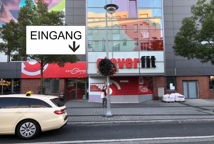 Ein Gebäude mit einem Schild mit der Aufschrift "City Center" und einem weiteren Schild mit der Aufschrift "Coverfit". Außerdem ist ein Auto am Straßenrand geparkt und eine Person steht in der Nähe des Eingangs des Gebäudes.