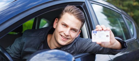 Junger Mann zeigt seinen Führerschein aus einem Auto lehnend