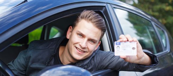 Junger Mann zeigt seinen Führerschein aus einem Auto lehnend