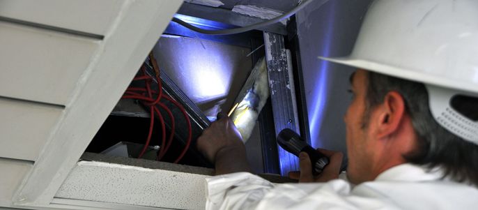 Arbeiter mit weißem Schutzhelm inspiziert Dämmmaterial in einem Kabelschacht.