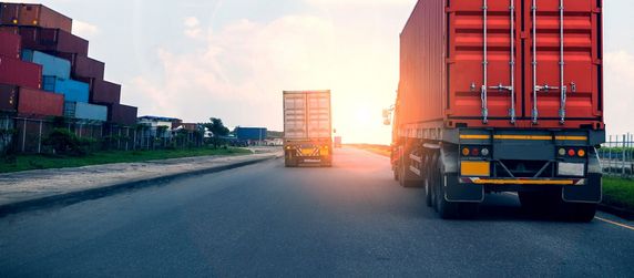 Mehrere LKWs die auf einer Straße neben einem Containerhof fahren