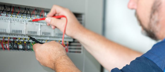 Ein Mann, der an einer elektrischen Schalttafel arbeitet und mit einem Schraubenzieher und einem Multimeter die Drähte überprüft.