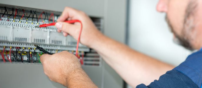 Ein Mann, der an einer elektrischen Schalttafel arbeitet und mit einem Schraubenzieher und einem Multimeter die Drähte überprüft.