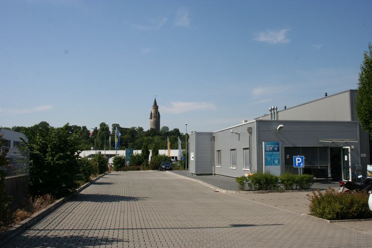 Ein modernes Gebäude mit einem blauen Schild, ein Parkplatz mit ein paar Autos und ein Turm im Hintergrund.