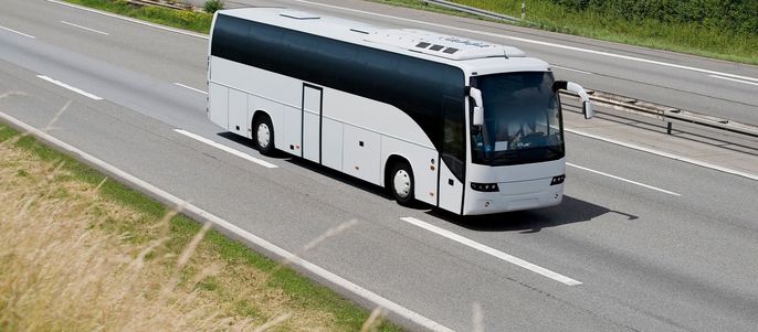 Ein weißer Reisebus, der auf einer Autobahn fährt, umgeben von Grünflächen auf beiden Seiten.