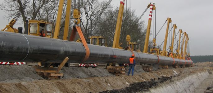 Ein großes Rohr wird von Kränen auf einer Baustelle transportiert.