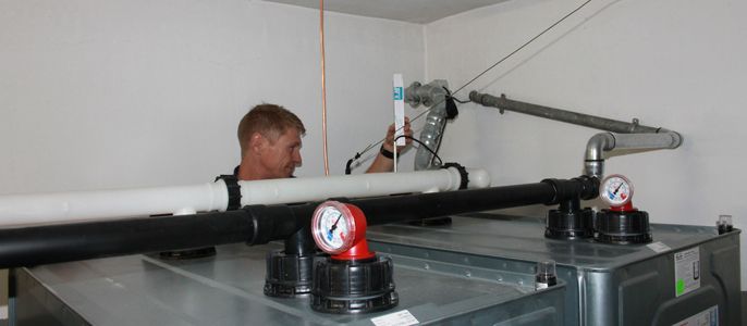Ein Mann arbeitet an einem Sanitärsystem mit verschiedenen Rohren, Ventilen und Messgeräten in einem Raum.