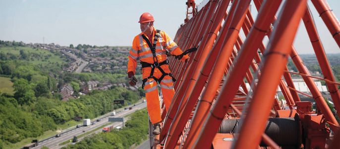Ein Bauarbeiter der auf einem Krahn steht.