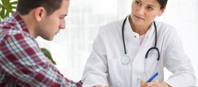 Eine medizinische Fachkraft, vermutlich ein Arzt, im Gespräch mit einem Patienten. Der Arzt schreibt etwas auf ein Blatt Papier, während der Patient aufmerksam zuhört.