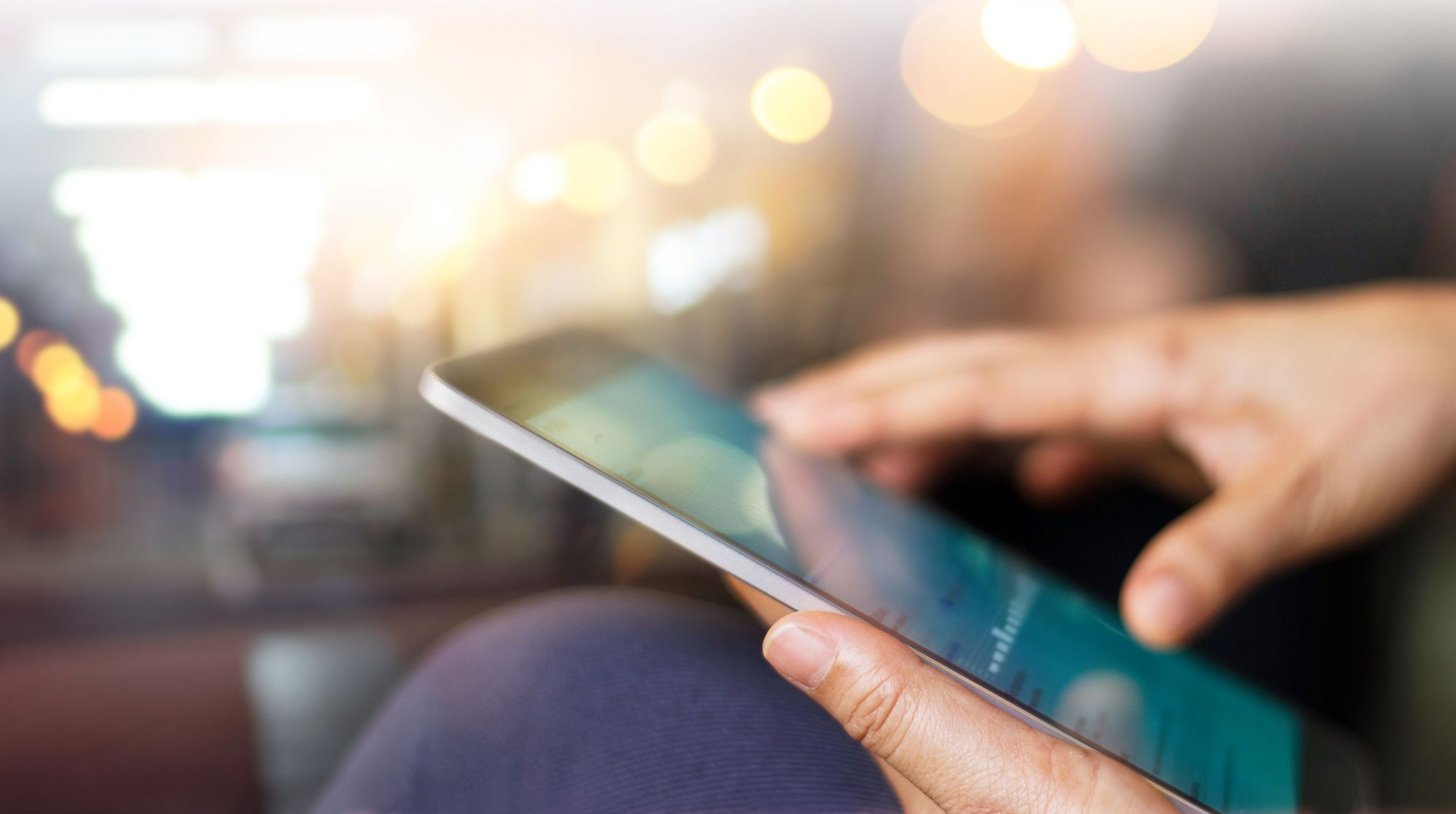 Die Hand einer Person, die ein Tablet hält, auf dessen Bildschirm ein Inhalt angezeigt wird.