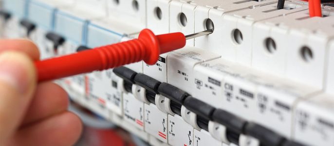 Nahaufnahme einer elektrischen Schalttafel mit mehreren Schaltern und Sicherungen, wobei eine Hand einen roten Schraubendreher benutzt, um einen der Schalter zu überprüfen.