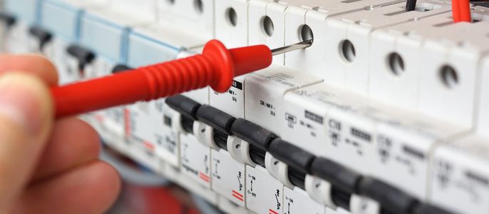 Nahaufnahme einer elektrischen Schalttafel mit mehreren Schaltern und Sicherungen, wobei eine Hand einen roten Schraubendreher benutzt, um einen der Schalter zu überprüfen.