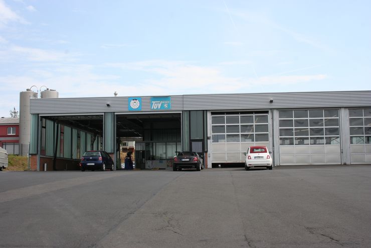 Eine moderne Garage mit drei großen Toren, einem blauen Schild mit dem Schriftzug "TUEV Hessen" und einigen davor geparkten Autos.