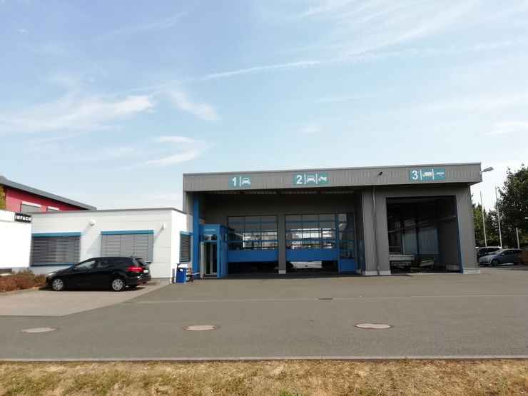 Ein modernes Gebäude mit blau-weißer Fassade, beschriftet mit den Zahlen "1", "2" und "3". Draußen ist ein Auto geparkt, und der Himmel ist klar mit ein paar Wolken.