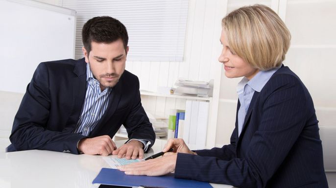 Zwei Fachleute, ein Mann und eine Frau, diskutieren an einem Tisch.