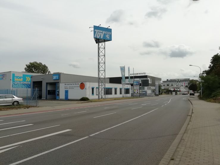 Eine Straßenansicht eines Gewerbegebiets mit einem auffälligen "TUEV Hessen"-Schild, einem Autoservice-Center und verschiedenen anderen Geschäften.