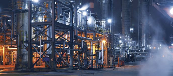 Eine nächtliche Industrieumgebung mit verschiedenen Maschinen und Strukturen, die von hellen Lichtern beleuchtet werden.