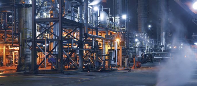 Ein industrielles Umfeld mit verschiedenen Maschinen und Geräten, beleuchtet von hellen Lichtern, die eine dunstige Atmosphäre erzeugen.