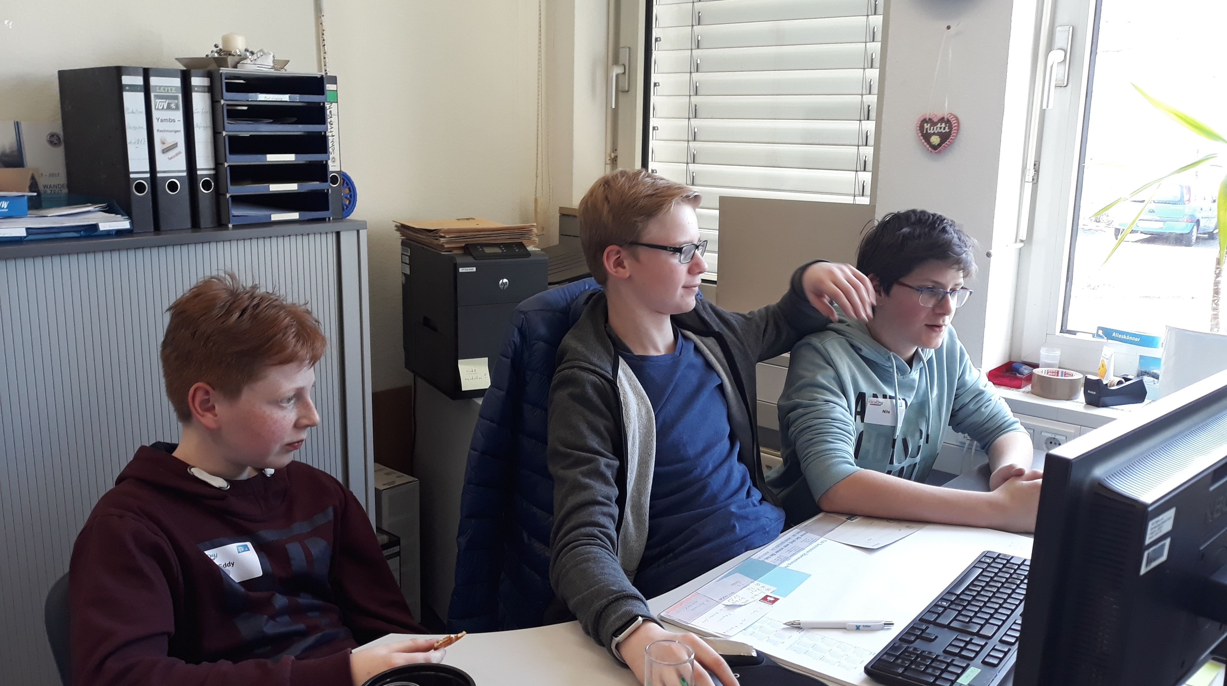 Drei Jungen in einem Büro, schauen konzentriert auf einen Computerbildschirm.