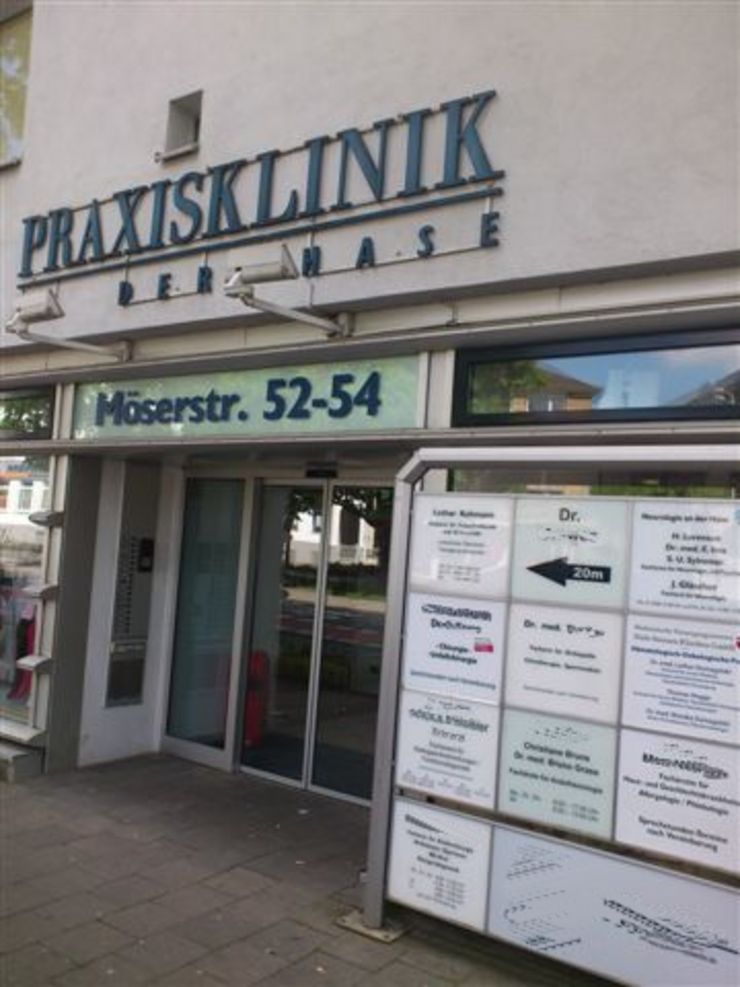 Ein Gebäude mit dem Schild "PRAXISKLINIK" über dem Eingang. Unterhalb befinden sich mehrere kleinere Schilder mit Text und anderen Informationen.