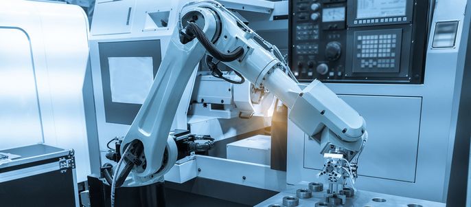 Ein Roboterarm in einer Fabrikumgebung, der mit einer Maschine interagiert.