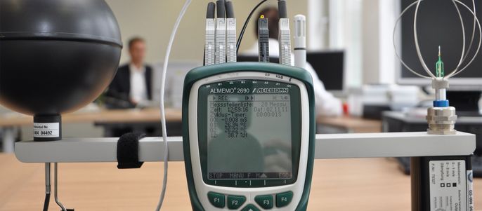 Ein Handheld-Gerät, an das verschiedene Kabel angeschlossen sind und das auf einem Tisch in einem Büro steht.
