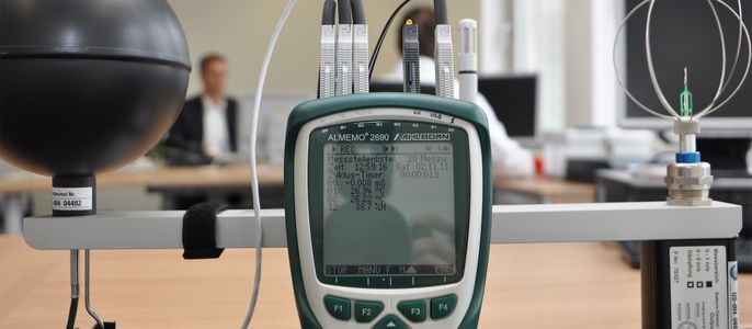 Ein Handheld-Gerät, an das verschiedene Kabel angeschlossen sind und das auf einem Tisch in einem Büro steht.
