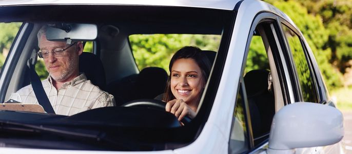Ein Mann und eine Frau in einem Auto, wobei die Frau fährt und der Mann auf eine Zeitung schaut.
