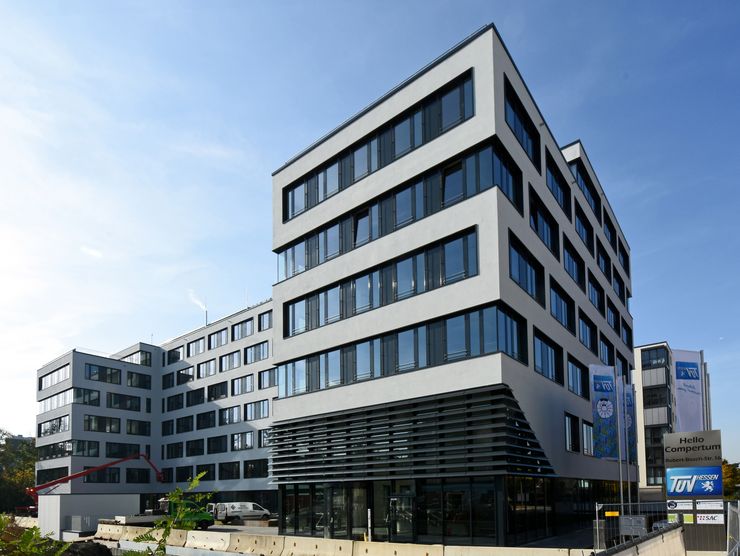 Ein modernes, mehrstöckiges Gebäude mit einer überwiegend weißen Fassade, zahlreichen Fenstern und einigen Werbungen an der Seite.