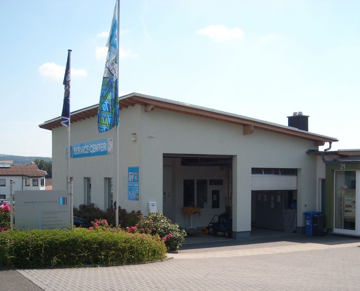 Ein Gebäude mit der Aufschrift "SERVICE-CENTER" mit einer blauen Fahne mit dem TUEV Hessen Logo und einem Hinweisschild.