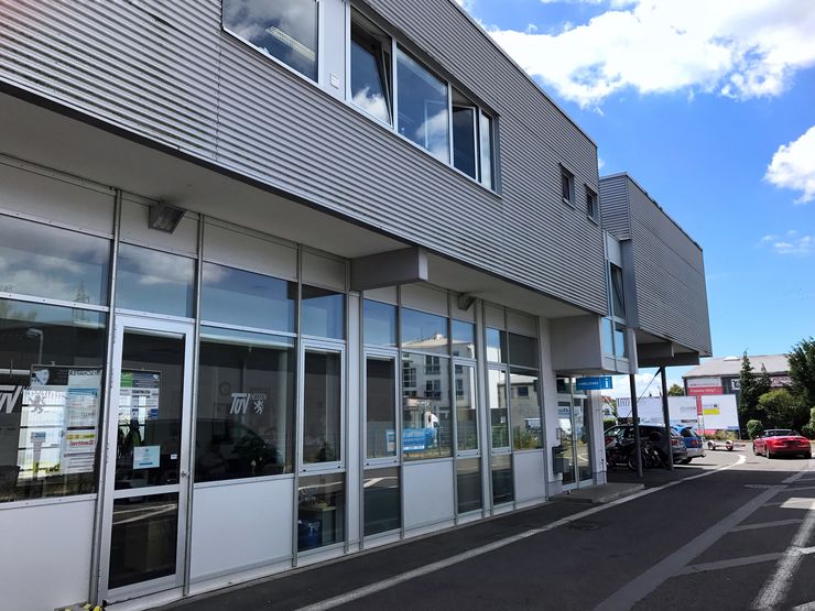 Ein modernes Gebäude mit großen Glasfenstern, ein blauer Himmel mit Wolken und ein paar Autos, die draußen parken.