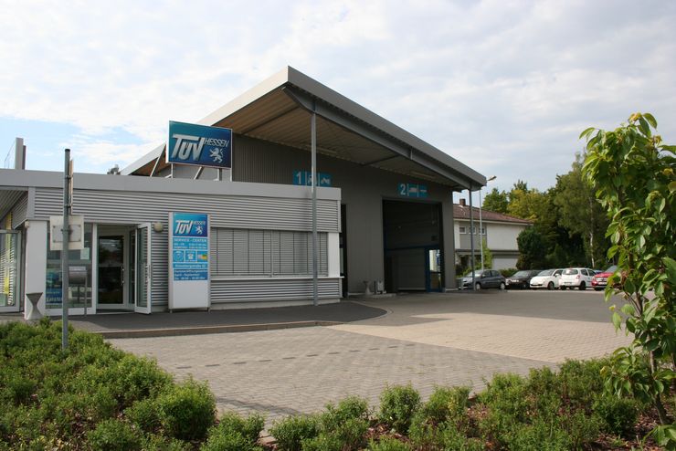 Eine moderne Autowaschanlage mit dem Namen "TUEV HESSEN", mit einem blauen Schild, einem gläsernen Eingang und einem Parkplatz voller Autos.