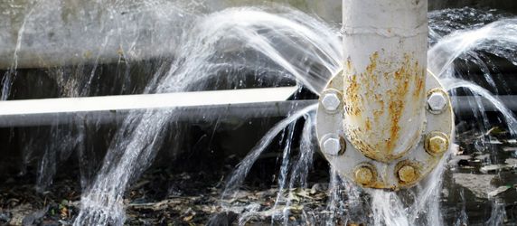 Ein weißes Rohr, aus dem Wasser sprudelt, umgeben von Trümmern und einer Betonstruktur.