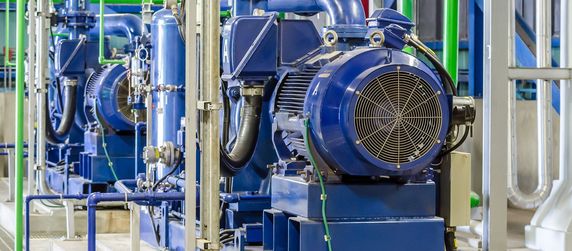 Eine Reihe von blauen Industriemaschinen, darunter große Elektromotoren und Rohre, in einer Fabrikumgebung.