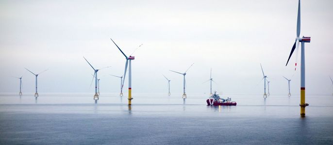 Eine weite, ruhige Wasserfläche mit mehreren Windturbinen, die sich am Horizont erheben, und einem Boot, das zwischen ihnen hindurchfährt.