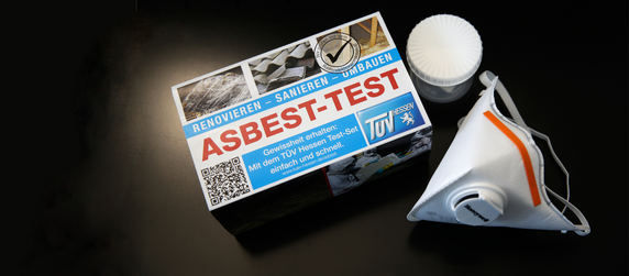 Eine Schachtel mit der Aufschrift 'RENOVIEREN - SANIEREN - UMBAUEN' und dem Titel 'ASBEST-TEST'. Daneben liegt eine weiße FFP-2 Maske.