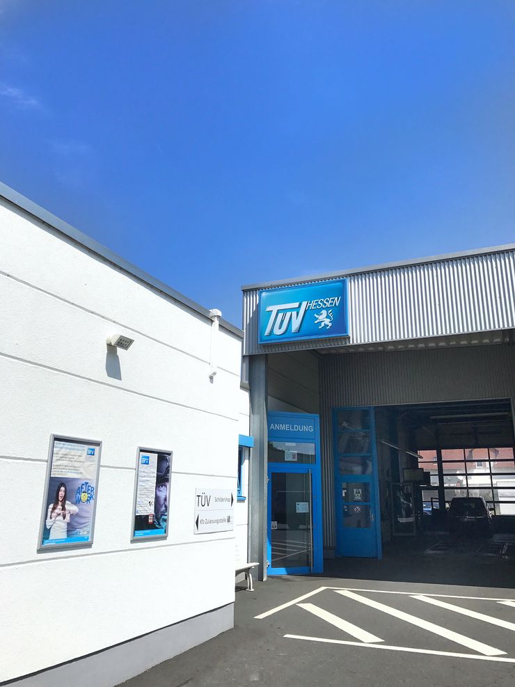 Ein Gebäude mit dem TUEV Hessen-Logo an der Fassade, einer blauen Tür und ein paar Plakaten an der Wand.