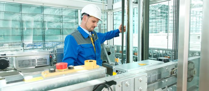 Ein Mann in blauer Uniform und weißem Schutzhelm bedient eine Maschine in einer modernen Industrieumgebung.
