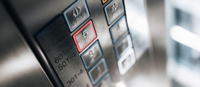 Eine Reihe von Tasten auf einer Aufzugstafel, wobei eine Taste rot hervorgehoben ist.