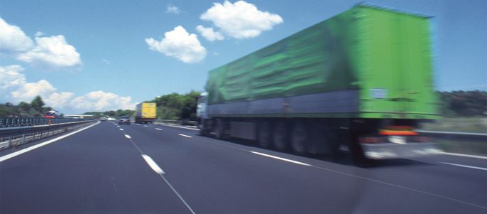 Eine Autobahn mit drei Lastwagen in Bewegung, unter einem klaren blauen Himmel mit ein paar Wolken.
