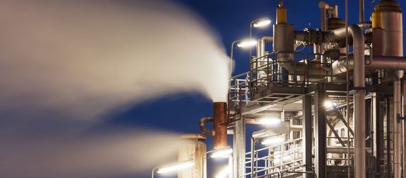 Eine nächtliche Industrieanlage mit dampfenden Maschinen vor einem dunklen Himmel.