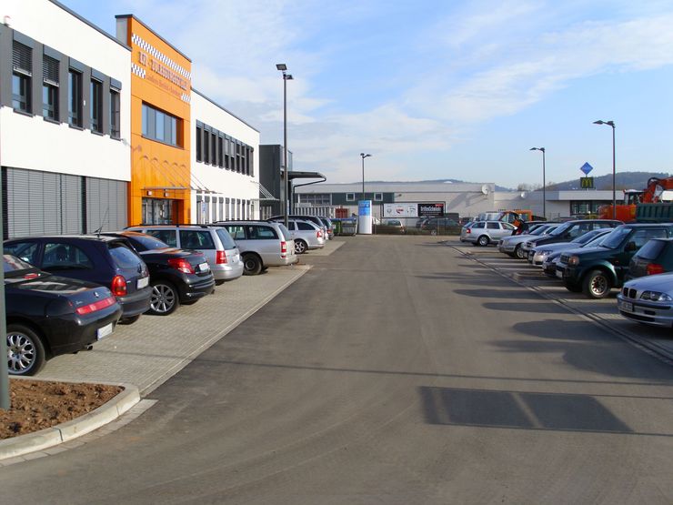 Ein Parkplatz, auf dem mehrere Autos in Reihen geparkt sind, mit einem Gebäude im Hintergrund, auf dem das Wort "Autohaus" steht.